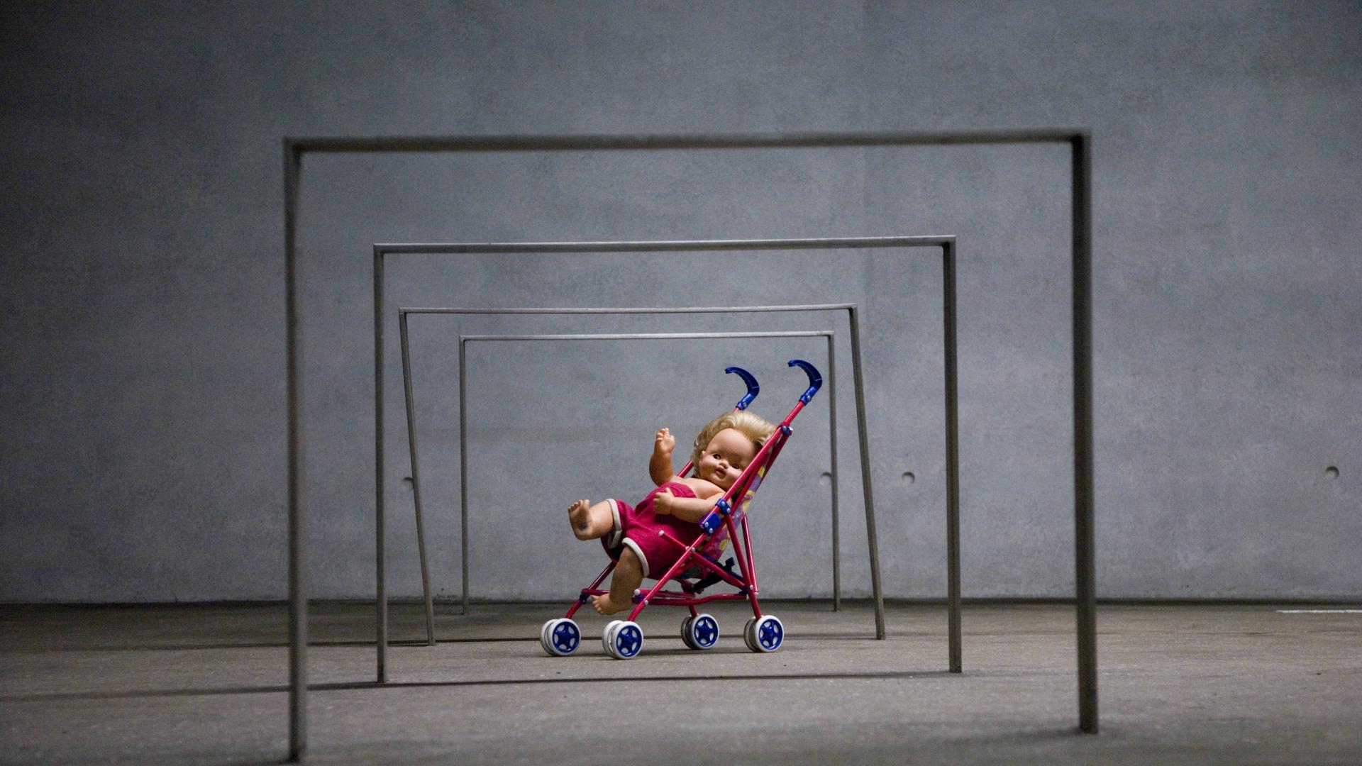 Puppe in einem Spielzeug-Kinderwagen unter eisernen Stangen, Kunstinstallation Puppe in einem Spielzeug-Kinderwagen unter eisernen Stangen, Kunstinstallation