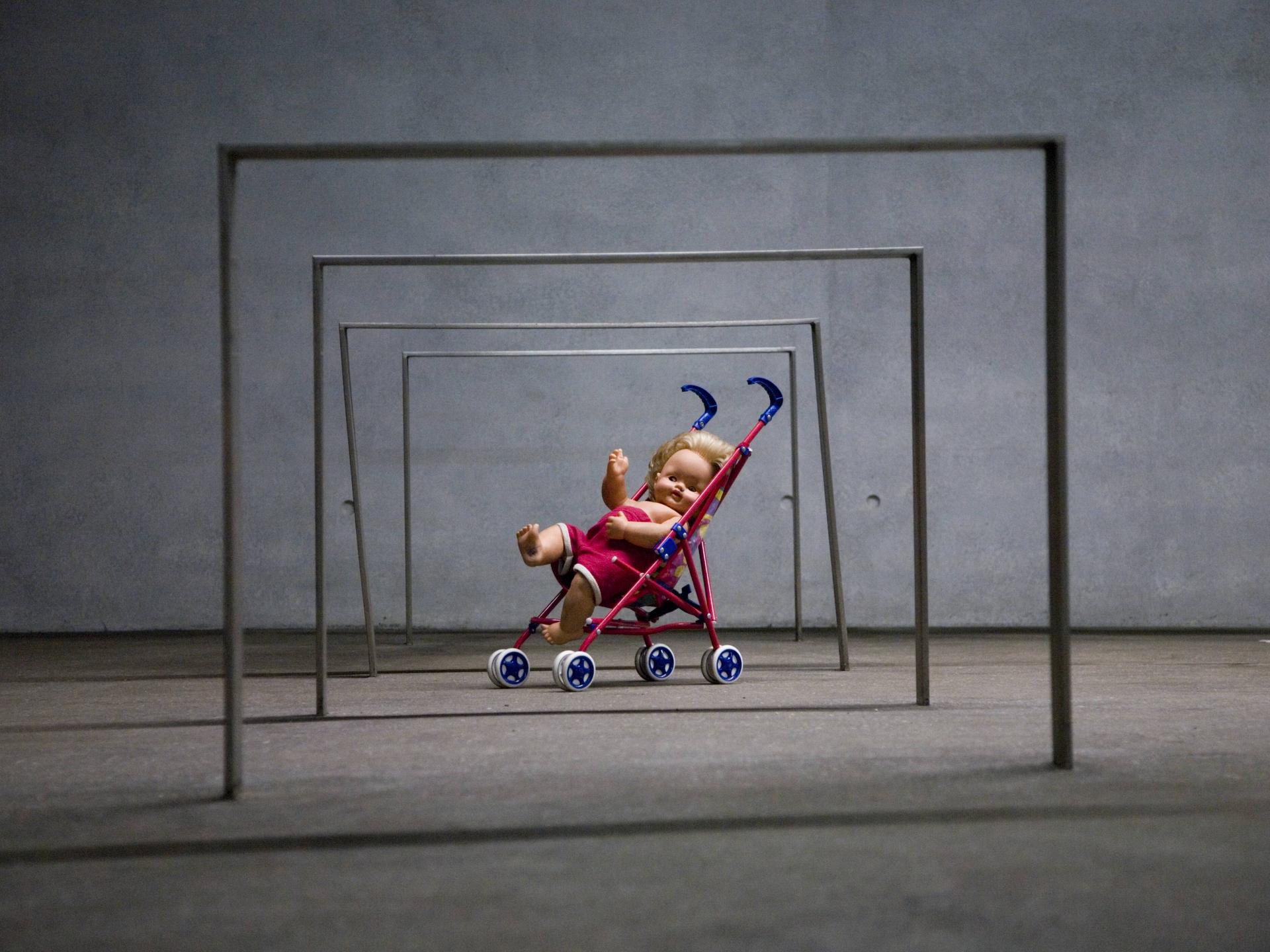 Puppe in einem Spielzeug-Kinderwagen unter eisernen Stangen, Kunstinstallation