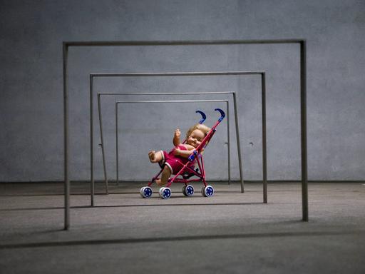 Puppe in einem Spielzeug-Kinderwagen unter eisernen Stangen, Kunstinstallation