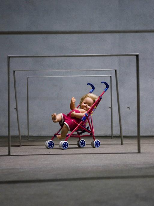 Puppe in einem Spielzeug-Kinderwagen unter eisernen Stangen, Kunstinstallation