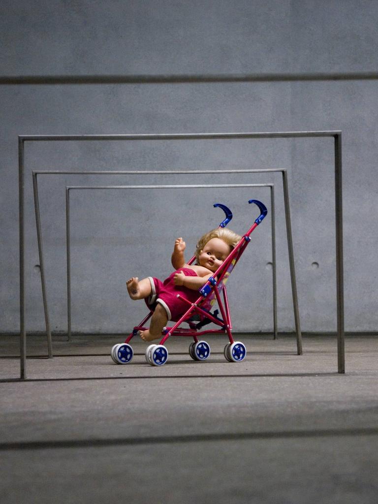 Puppe in einem Spielzeug-Kinderwagen unter eisernen Stangen, Kunstinstallation