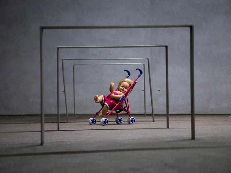 Puppe in einem Spielzeug-Kinderwagen unter eisernen Stangen, Kunstinstallation