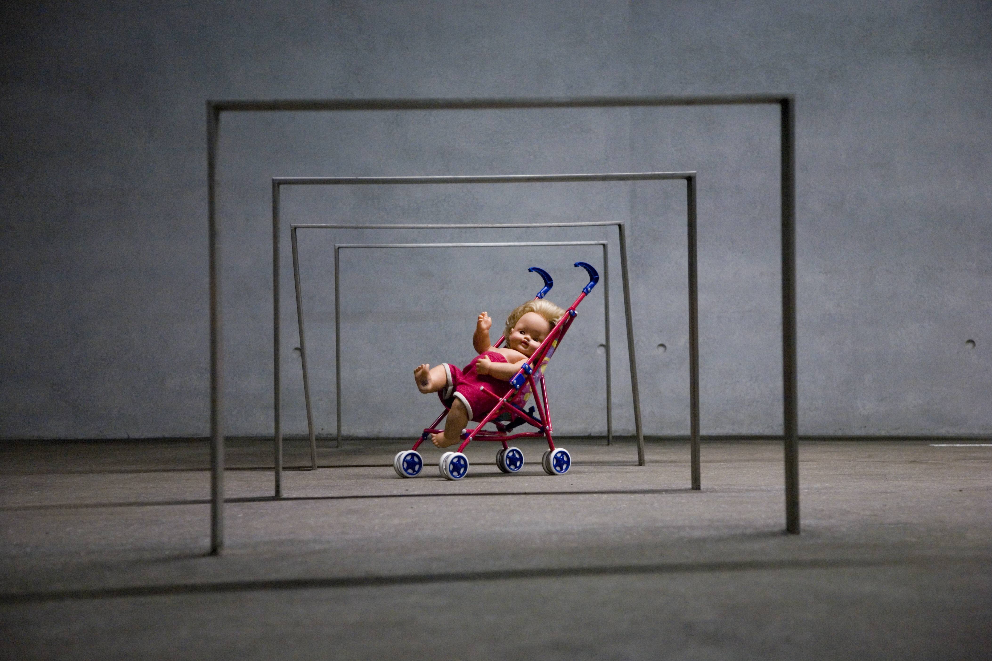 Puppe in einem Spielzeug-Kinderwagen unter eisernen Stangen, Kunstinstallation