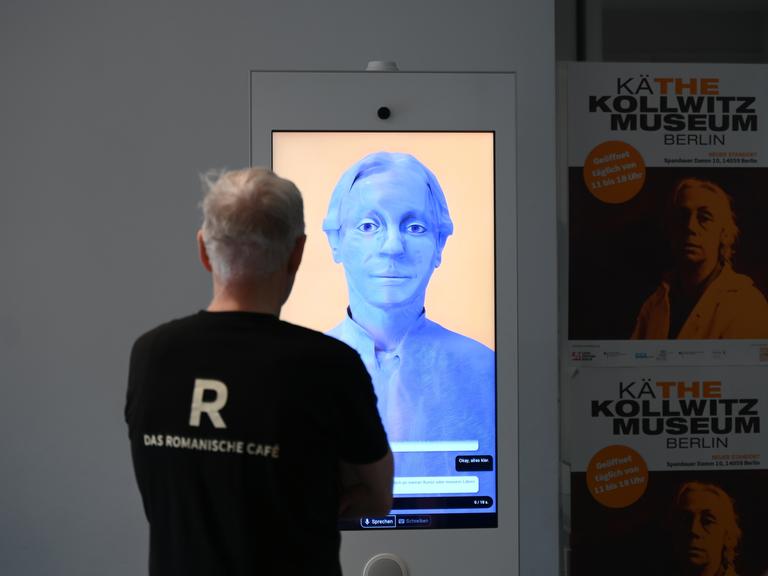 Ein Besucher steht im Käthe-Kollwitz-Museum mit einem mit 3D-Animation und künstlicher Intelligenz hergestellten digitalen Avatar in der Gestalt von Käthe Kollwitz.