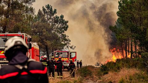 Waldbrand in der Gironde im Juli 2026. Links sind Feuerwehrautos und Feuerwehrleute zu sehen, rechts Flammen im Wald.
