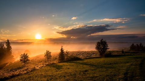 Ein Sonnenuntergang in bergiger Landschaft, die in rötliche Farben getaucht ist.