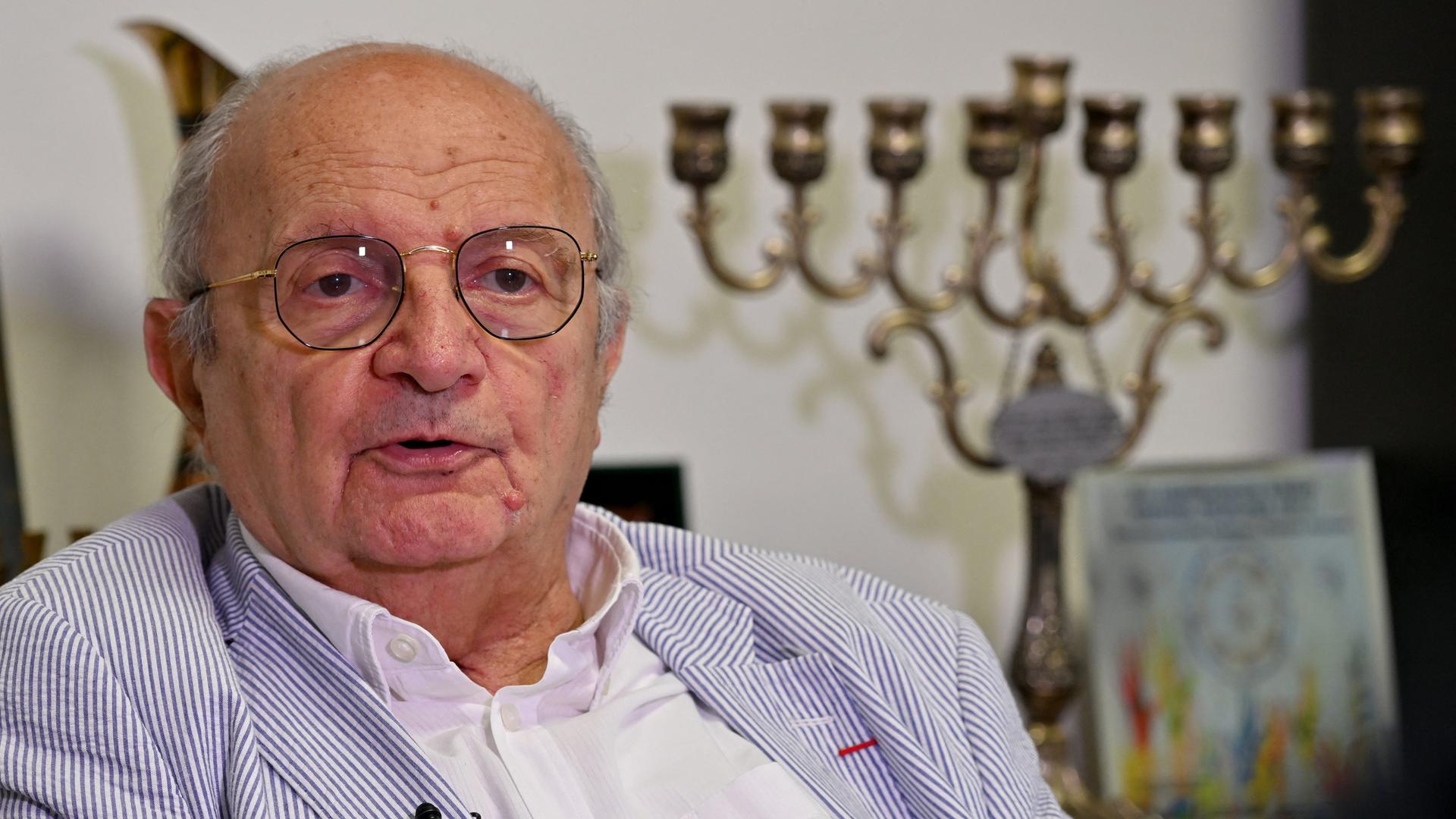 Jakob Finci ist ein älterer Herr mit Brille und Halbglatze. Er trägt einen Anzug mit schmalen blau-weißen Streifen.