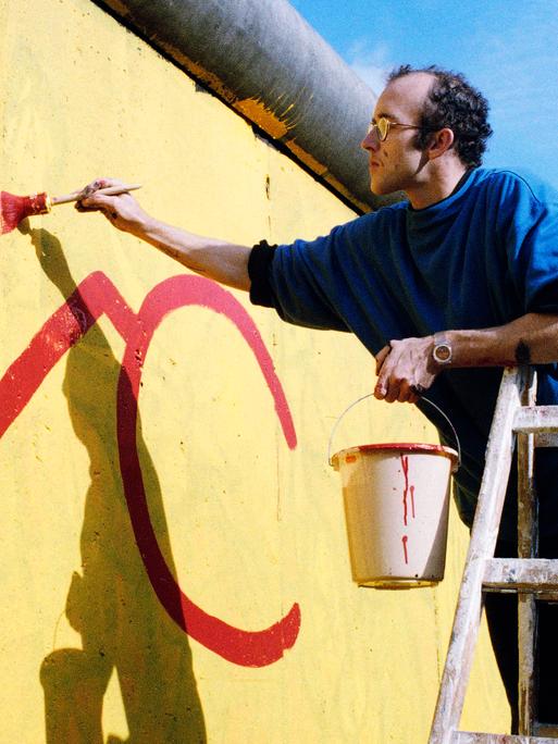Der US-Künstler Keith Haring malt einen Teil der Berliner Mauer im Jahr 1986 an.
