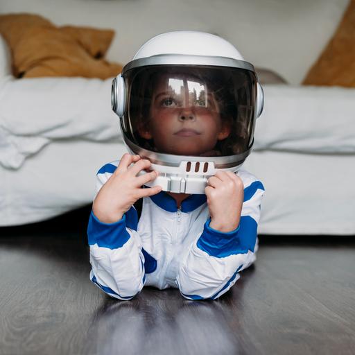 Ein Kind liegt in einem Astronautenkostüm auf dem Boden vor einem Sofa und guckt verträumt.