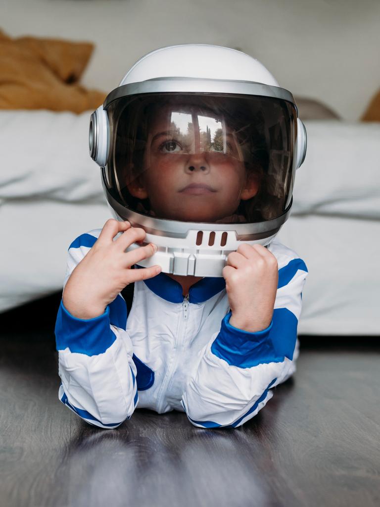 Ein Kind liegt in einem Astronautenkostüm auf dem Boden vor einem Sofa und guckt verträumt.