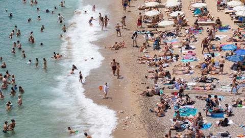 An einem Strand der kroatischen Stadt Dubrovnik liegen Toristinnen und Touristen am Strand und baden im Meer.