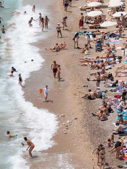 An einem Strand der kroatischen Stadt Dubrovnik liegen Toristinnen und Touristen am Strand und baden im Meer.