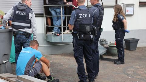 Schlag gegen mutmaßliche Menschenhändler: Bei dieser Razzia suchen Polizei und Zoll nach Menschen, die in teils unwürdigen Bedingungen leben. Zu sehen sind Zoll- und Polizeibeamte in Uniform. Sie stehen vor einem Gebäudeeingang. 