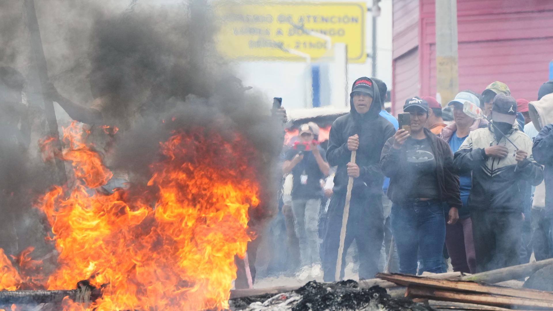 Demonstranten blockieren eine Straße in Ecuador. Im Vordergrund brennt ein Feuer. 
