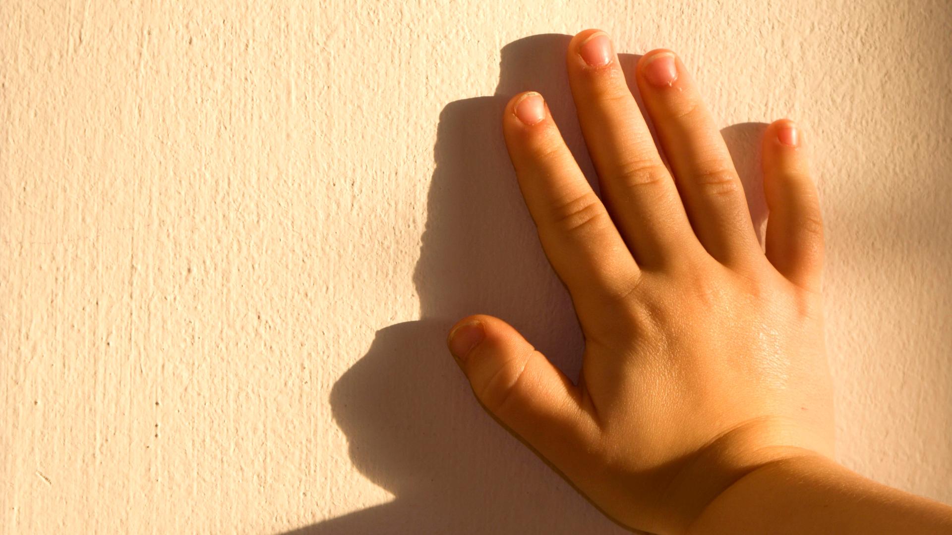 Die Hand eines Kindes drückt gegen eine Mauer
