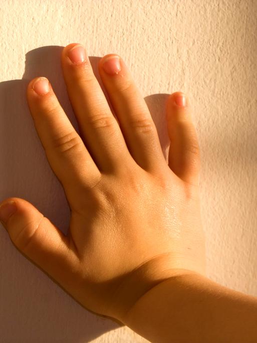 Die Hand eines Kindes drückt gegen eine Mauer