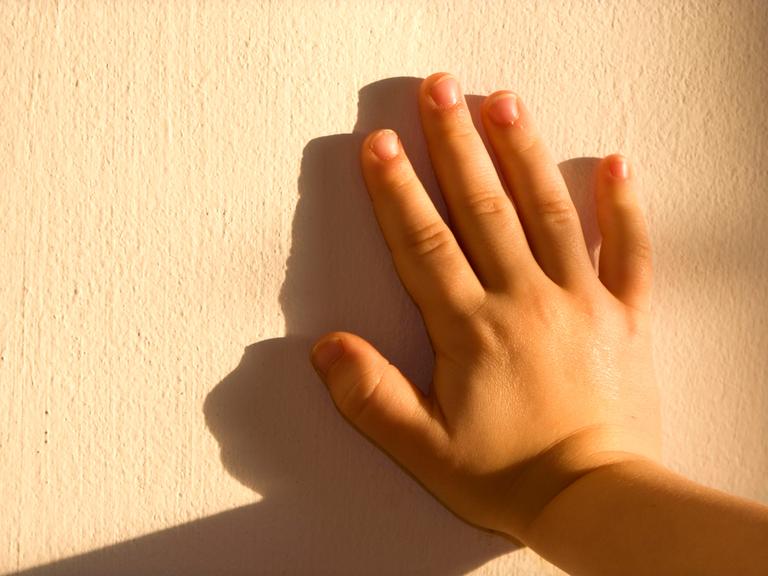 Die Hand eines Kindes drückt gegen eine Mauer