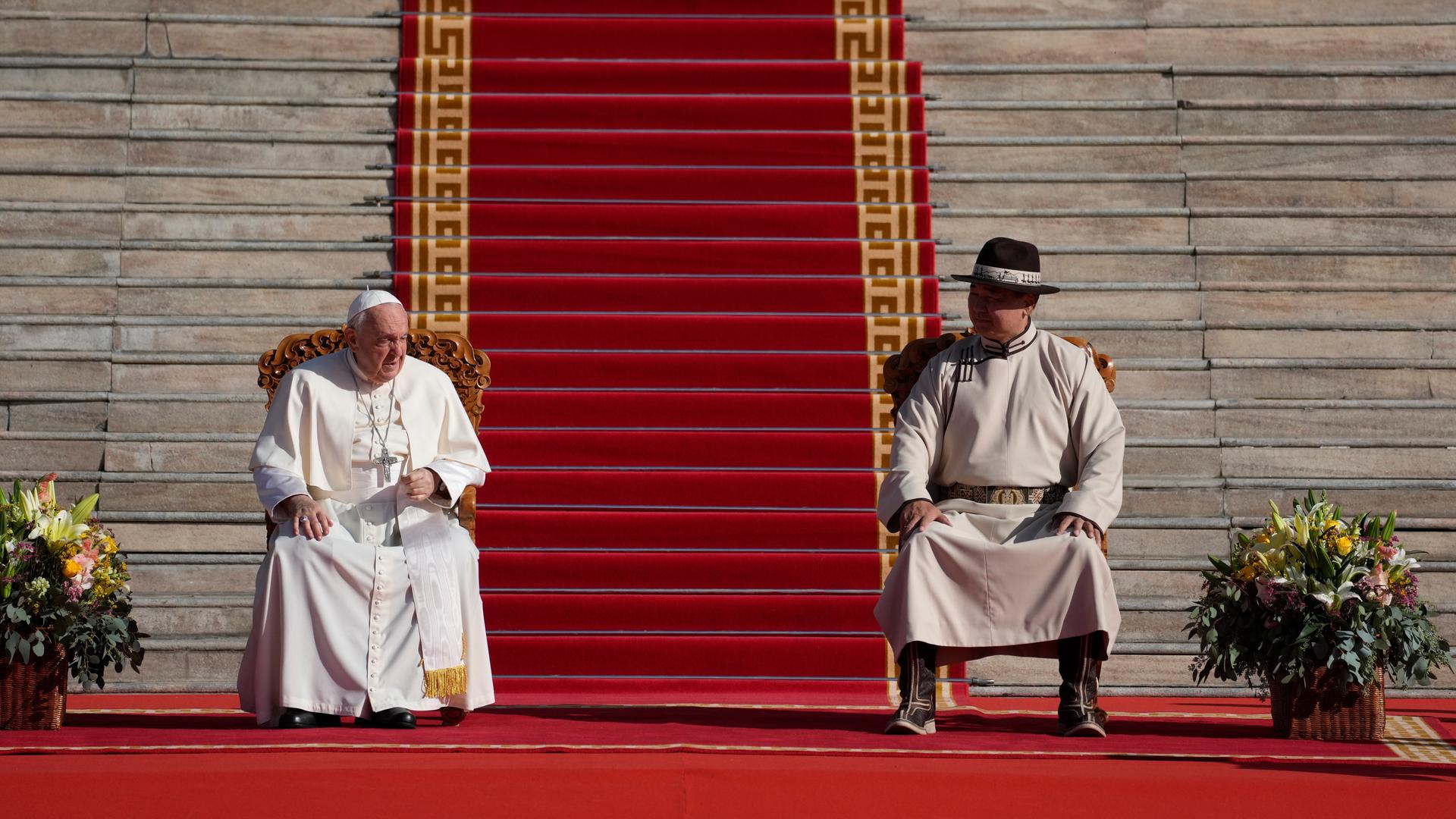 Papst Franziskus sitzt auf einem Stuhl, neben ihm der Präsident der Mongolei, Ukhnaagin Khurelsukh. Im Hintergrund ist eine Treppe. Der Platz davor ist mit einem roten Teppich geschmückt.