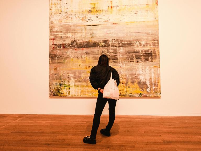 Eine Frau steht in einem Ausstellungsraum vor einem ungegenständlichen Gemälde.