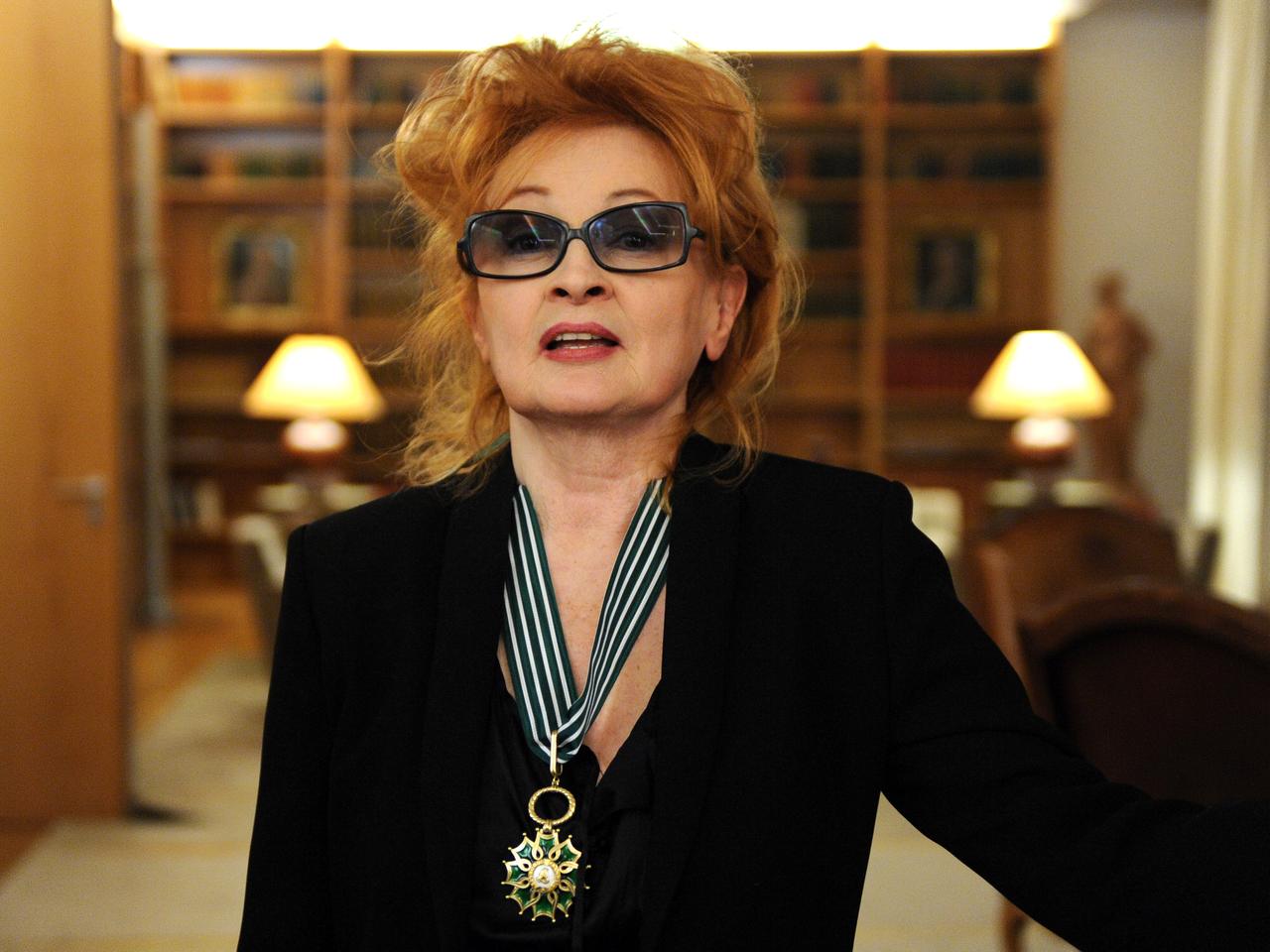 Ingrid Caven in der Französischen Botschaft mit Sonnenbrille im Gesicht und Orden um den Hals.