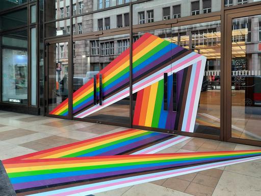 Die Fassade und der Gehweg von einem Gebäude sind mit Regenbogentape beklebt.