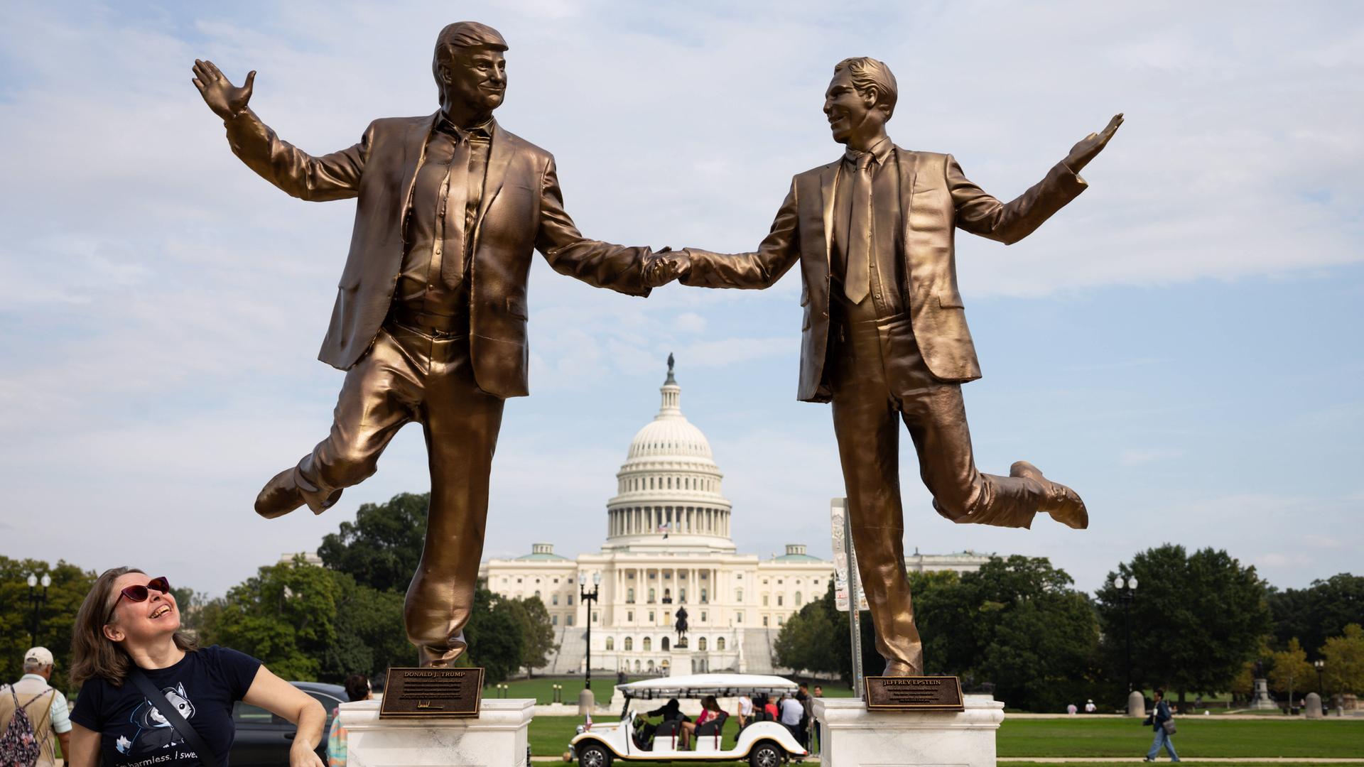 Eine Frau blickt auf Bronze farbene Statuen von US-Präsident Donald Trump und dem Sexualstraftäter Jeffrey Epstein, die sich an den Händen halten und vor dem Kapitol in Washington tanzen. 