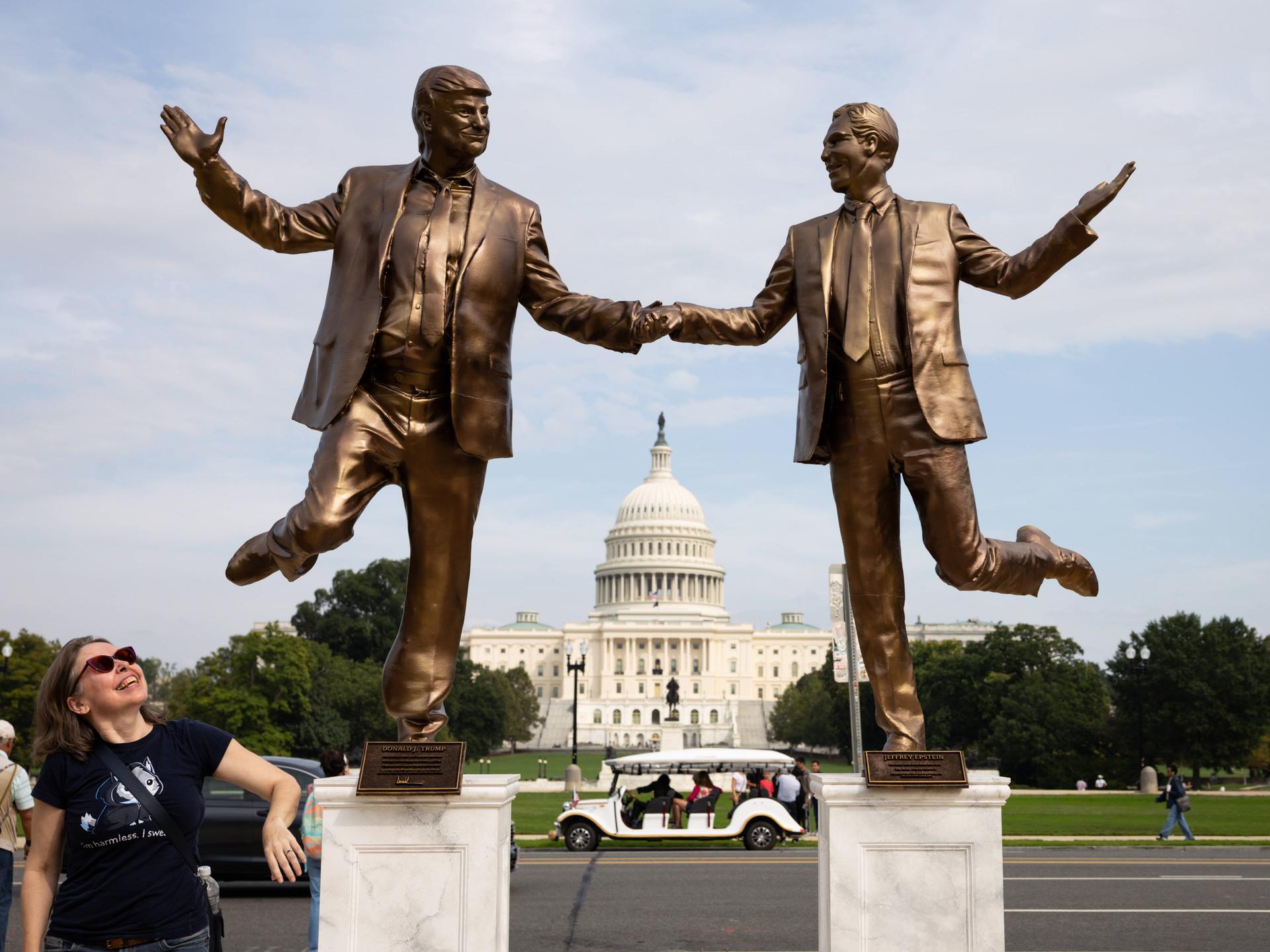 Eine Frau blickt auf Bronze farbene Statuen von US-Präsident Donald Trump und dem Sexualstraftäter Jeffrey Epstein, die sich an den Händen halten und vor dem Kapitol in Washington tanzen. 