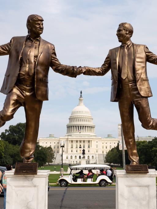 Eine Frau blickt auf Bronze farbene Statuen von US-Präsident Donald Trump und dem Sexualstraftäter Jeffrey Epstein, die sich an den Händen halten und vor dem Kapitol in Washington tanzen. 