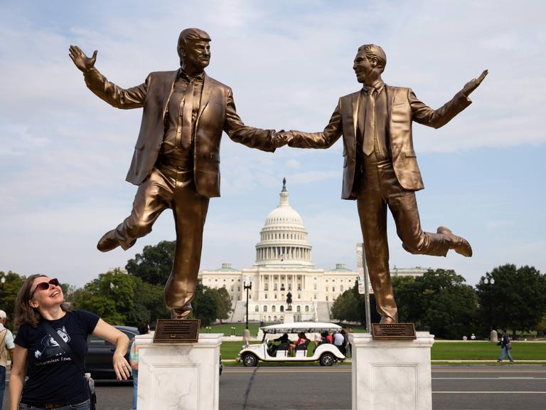 Eine Frau blickt auf Bronze farbene Statuen von US-Präsident Donald Trump und dem Sexualstraftäter Jeffrey Epstein, die sich an den Händen halten und vor dem Kapitol in Washington tanzen. 