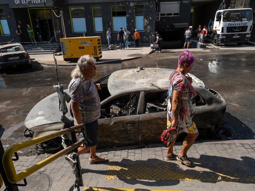 Nach russischen Angriffen mit Drohne und Rakete auf ein Wohnviertel gehen Bewohner an ausgebrannten Autos und beschädigten Häuserfassaden entlang.