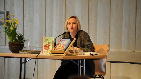 Ute Krause, deutsche Schriftstellerin und Illustratorin von Kinder- und Jugendbüchern bei einer Lesung. Sie sitzt an einem Tisch, trägt eine dunkle Jacke und vor ihr liegen und stehen einige ihrer Bücher.