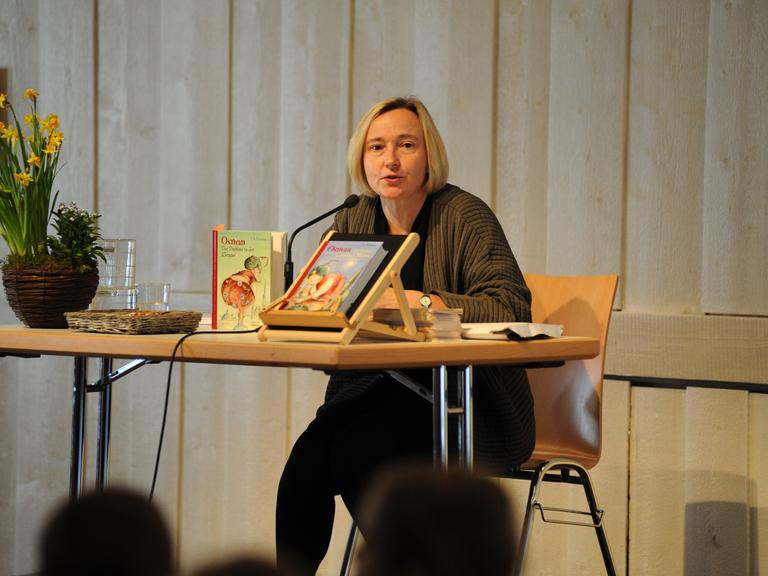 Ute Krause, deutsche Schriftstellerin und Illustratorin von Kinder- und Jugendbüchern bei einer Lesung. Sie sitzt an einem Tisch, trägt eine dunkle Jacke und vor ihr liegen und stehen einige ihrer Bücher.