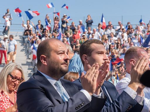 David Rachline applaudiert bei einer Veranstaltung. Im Hintergrund schwenken Menschen französische Flaggen.