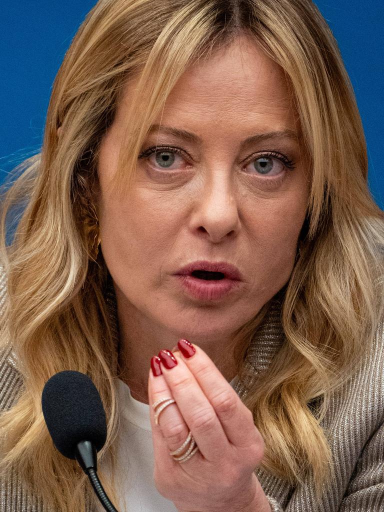 Giorgia Meloni, die Premierministerin Italiens, sitzt bei einer Pressekonferenz vor einem Mikrofon. Sie spricht und hält dabei die Hand in die Luft.
