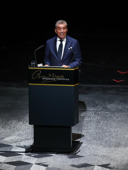 Michel Friedman steht in einer dunklen Umgebung an einem Redepult und spricht in ein Mikrofon.