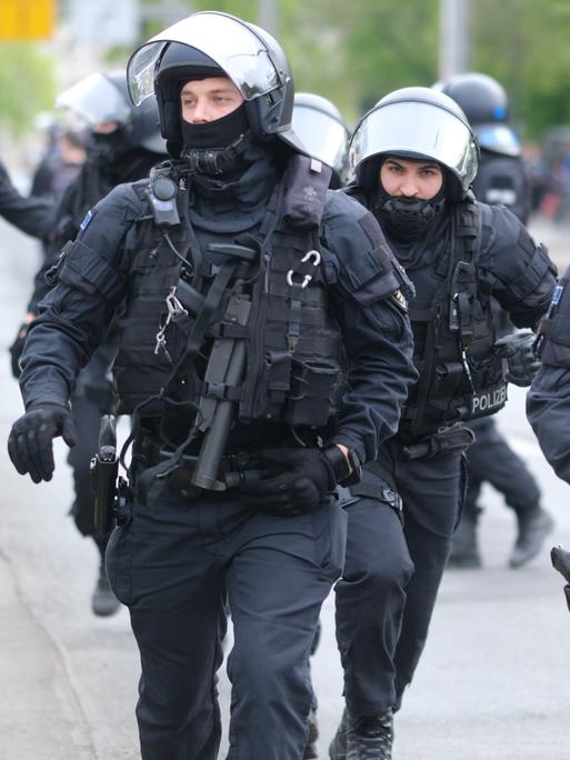 Polizisten mit Helmen und Schutzkleidung laufen eine Straße entlang.