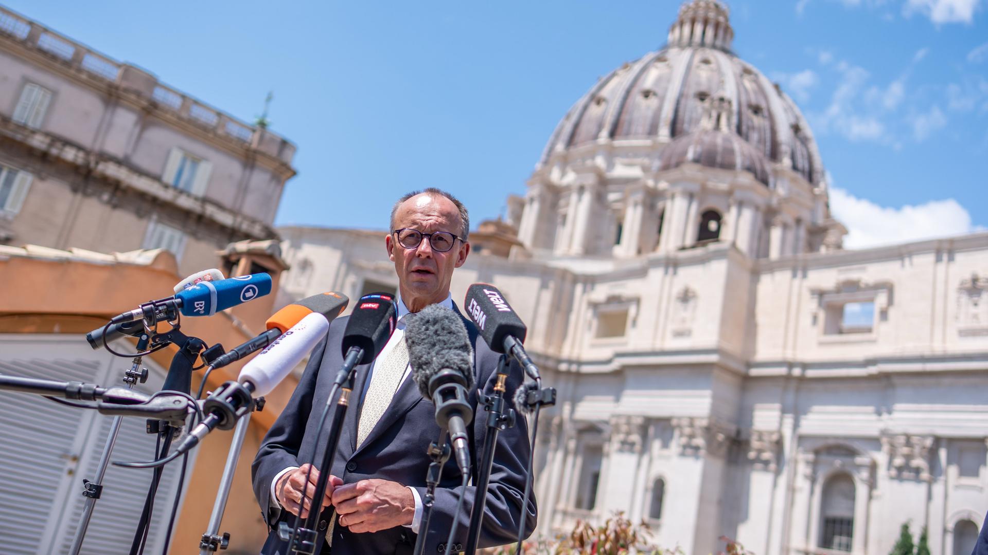 Bundeskanzler Friedrich Merz spricht nach der Amtseinführung von Papst Leo XIV in Mikrofone. Er steht auf dem Petersplatz im Vatikan.