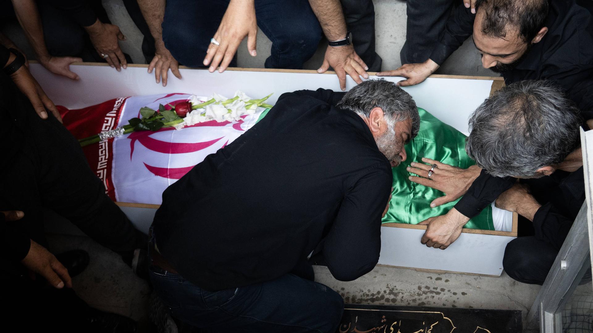 Ein Angehöriger trauert am Sarg über einen bei israelischen Angriffen getöteten Militärangehörigen. Das Opfer ist in die iranische Flagge gehüllt.

