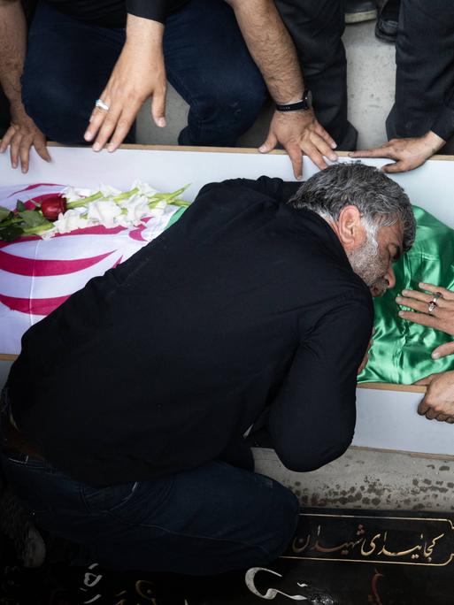 Ein Angehöriger trauert am Sarg über einen bei israelischen Angriffen getöteten Militärangehörigen. Das Opfer ist in die iranische Flagge gehüllt.

