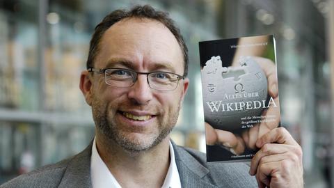 Jimmy Wales hält Buch „Alles über Wikipedia“ hoch.