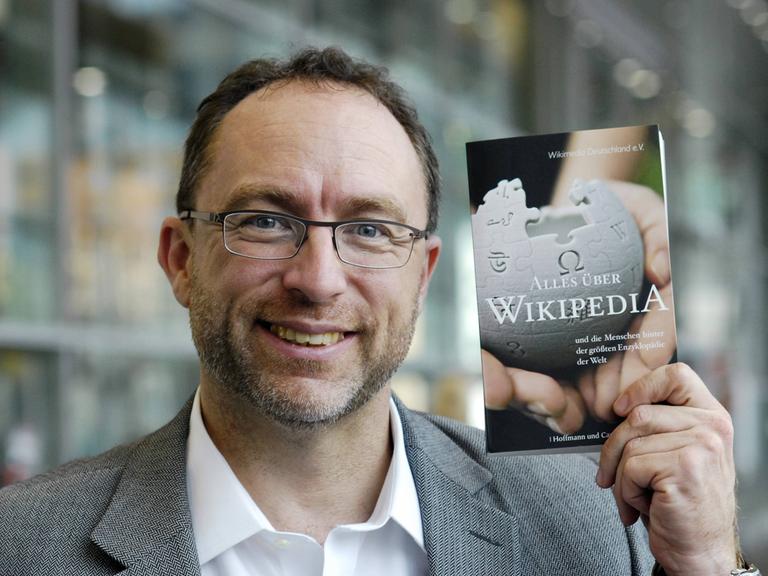 Jimmy Wales hält Buch „Alles über Wikipedia“ hoch.