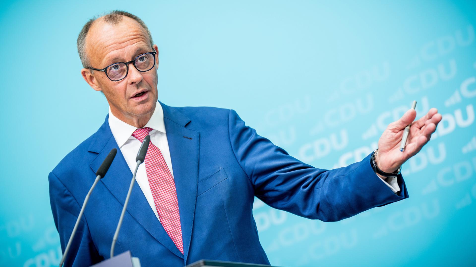 Friedrich Merz steht an einem Rednerpult und macht eine weit ausholende Geste mit seiner linken Hand, in der er einen Kugelschreiber hält.