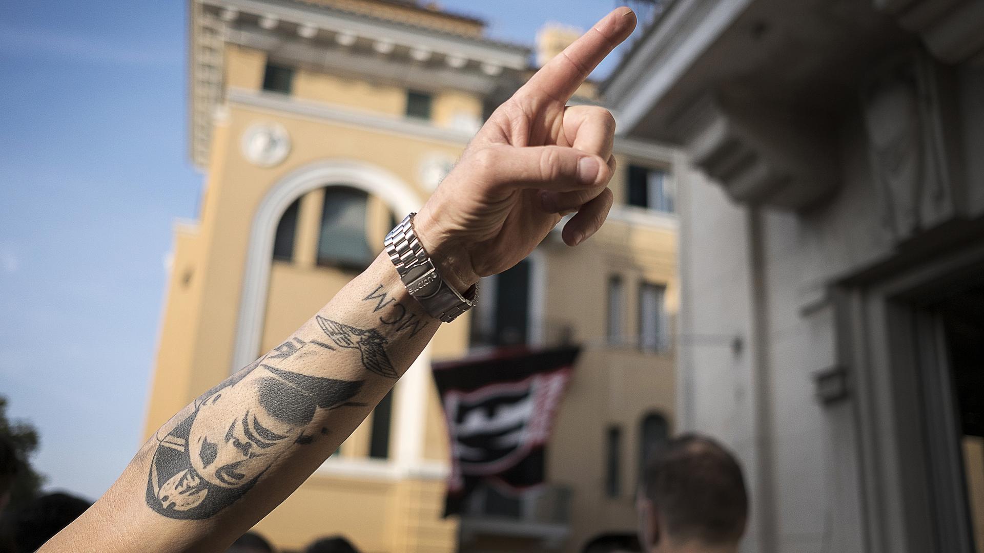 Aufnahme eines Armes mit erhobenem Zeigefinger und einem Tattoo mit dem Gesicht von Benito Mussolini.