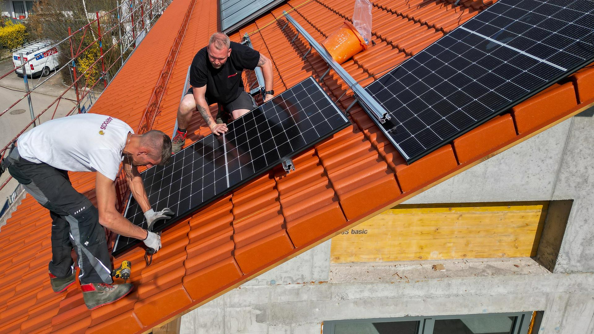 Zwei Arbeiter einer Montagefirma auf einem Dach bringen Photovoltaik-Module an. 