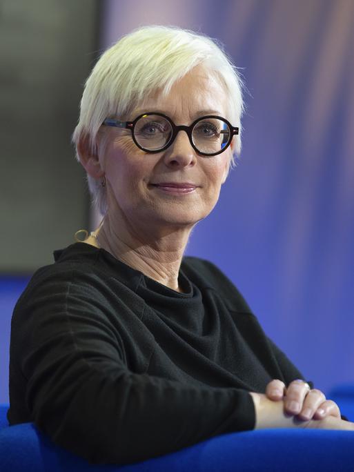 Die Schriftstellerin Dörte Hansen im Porträt mit hellblonden, kurzen Haaren und dunkler Brille vor blauem Hintergrund 