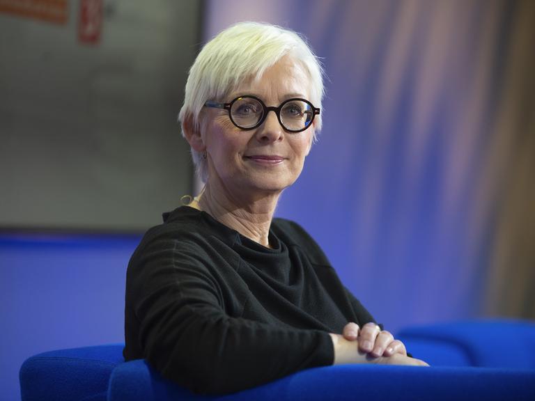 Die Schriftstellerin Dörte Hansen im Porträt mit hellblonden, kurzen Haaren und dunkler Brille vor blauem Hintergrund 