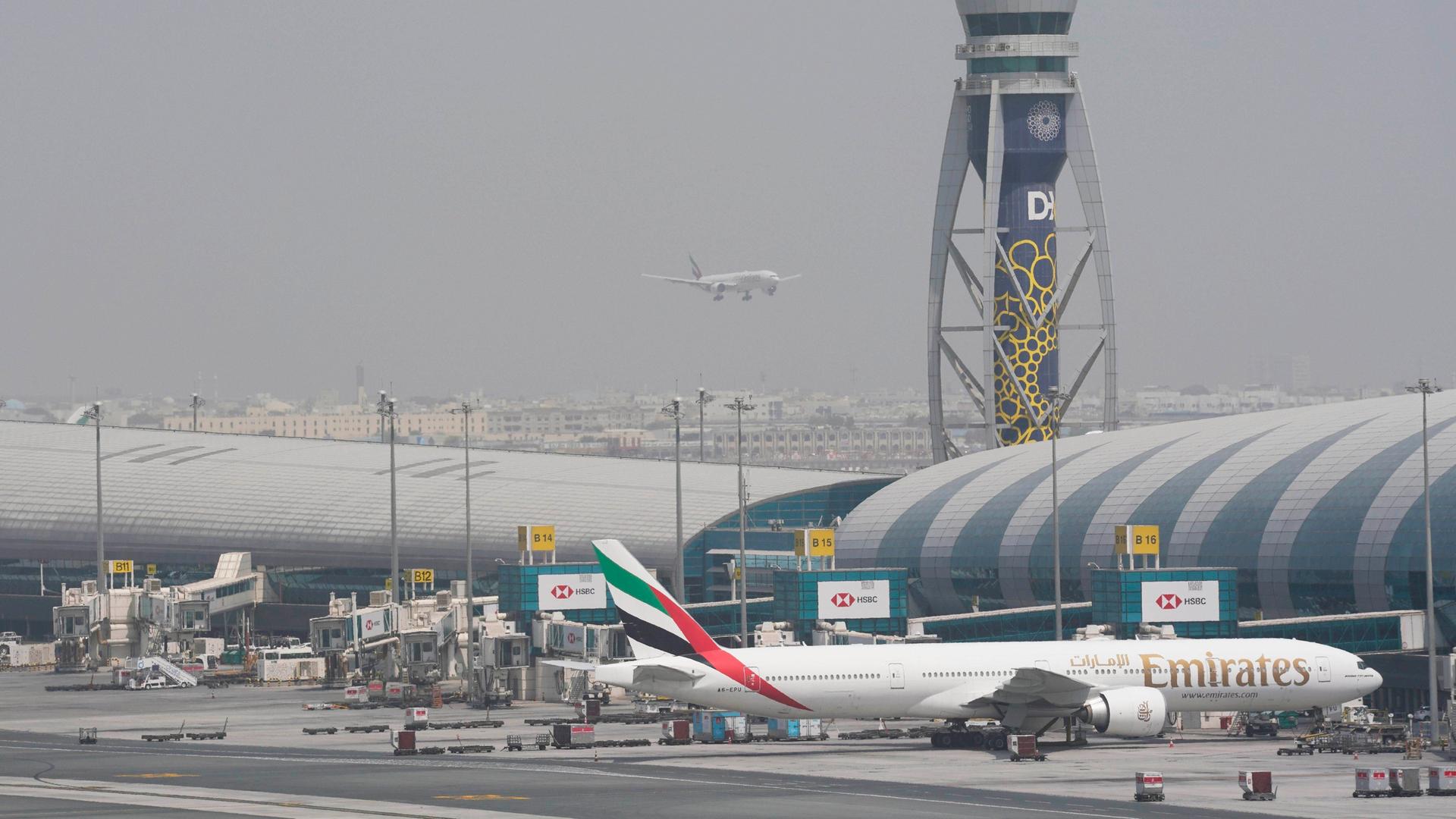 Eine Boeing 777 der Fluggesellschaft Emirates steht am Gate des internationalen Flughafens von Dubai, während sich eine andere Maschine auf die Landung auf der Startbahn vorbereitet.