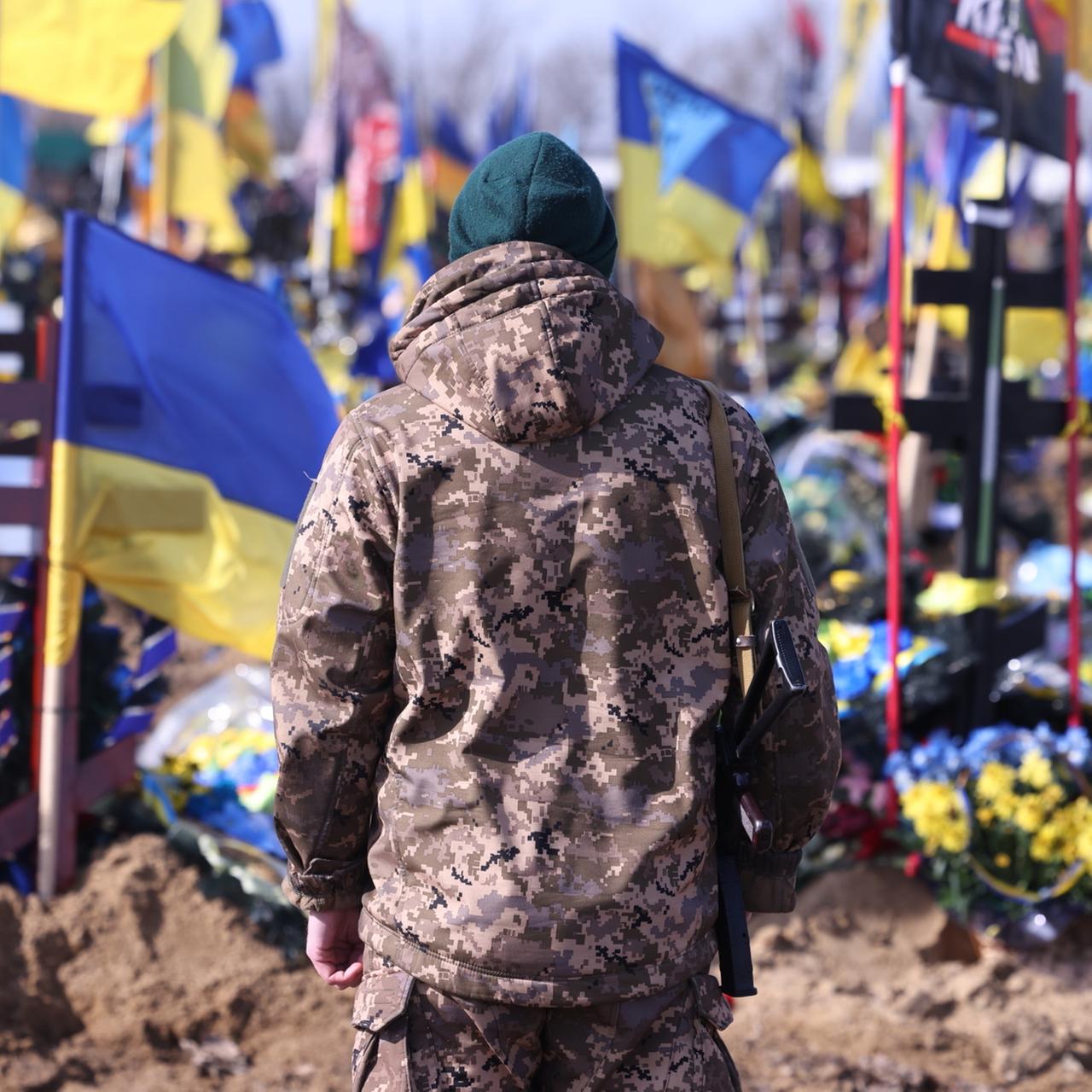 Ein Ukrainischer Soldat steht auf einem Friedhof in Kharkiw vor den Gräbern im Krieg gefallener ukrainischer Soldaten.