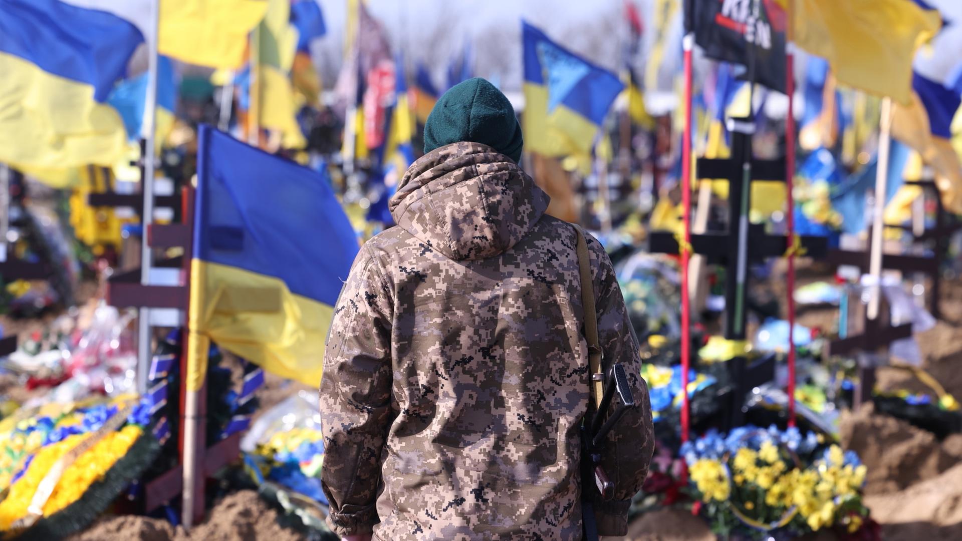 Ein Ukrainischer Soldat steht auf einem Friedhof in Kharkiw vor den Gräbern im Krieg gefallener ukrainischer Soldaten.