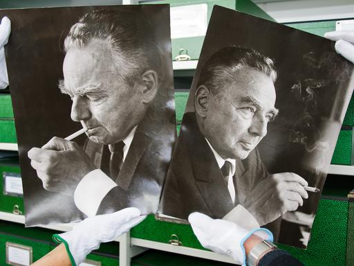 Im Literaturarchiv in Marbach halten zwei Mitarbeitenden, von denen Mann nur die Hände sieht, zwei Bilder in die Höhe, die den Schriftsteller Erich Kästner zeigen. 